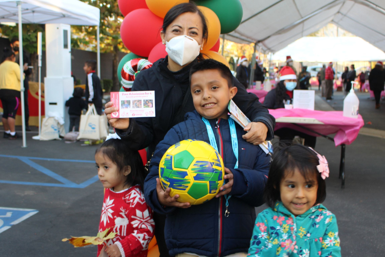 A mother holds a grocery gift card while surrounded by her three children who have just received toys at a local toy giveaway. 