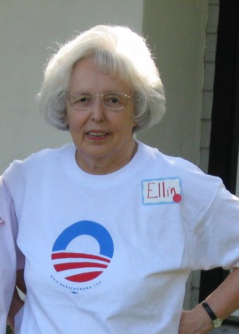 An older woman with gray hair wears a white t-shirt with a red and blue logo for the 2008 Obama campaign t-shirt and a nametag that reads Ellin.