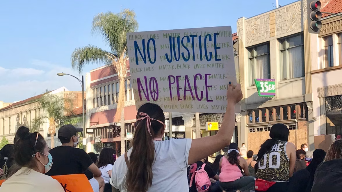 A woman holds a sign in a crowd that reads No Justice No Peace