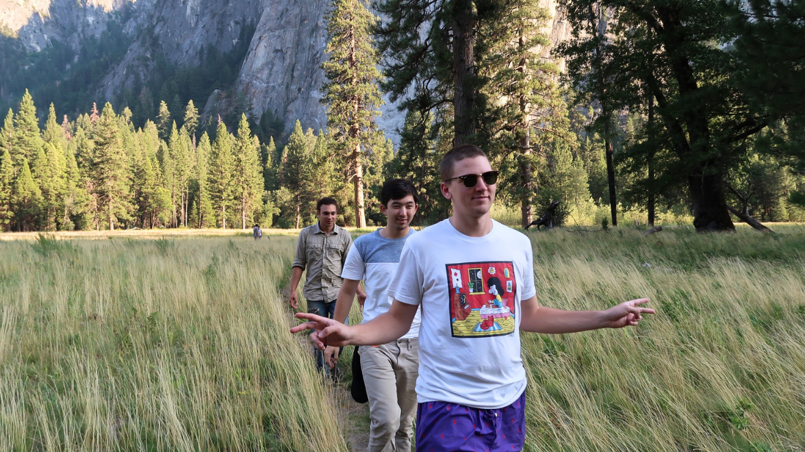 Three young men walk through a Yosemite meadow with large mountains behind them