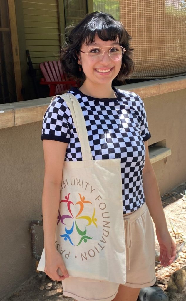 Emily, a 2021-22 PCF Scholar with Pasadena Community Foundation, stands outdoors wearing a checkered shirt and carrying a Pasadena Community Foundation tote bag. . 