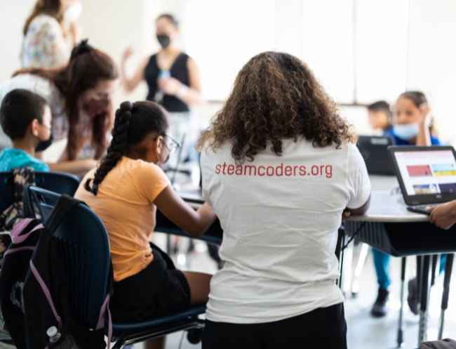 A young student at a computer works with a volunteer from the STEAM:CODERS organization in Pasadena