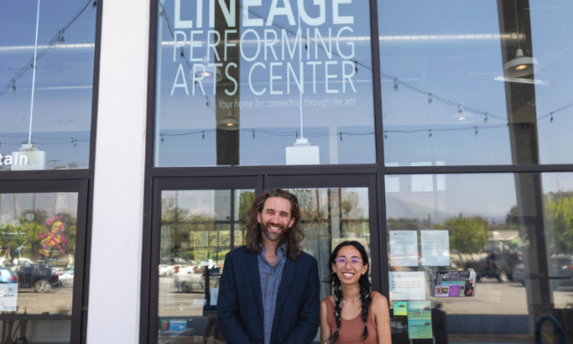 A man and a woman stand outside glass doors and windows with a sign that reads Lineage Performing Arts Center.