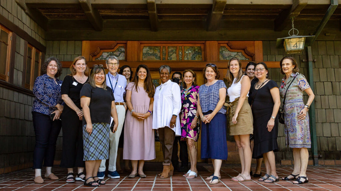 A large group of people pose on a brick porch with beautiful rich colored wood doorway behind them