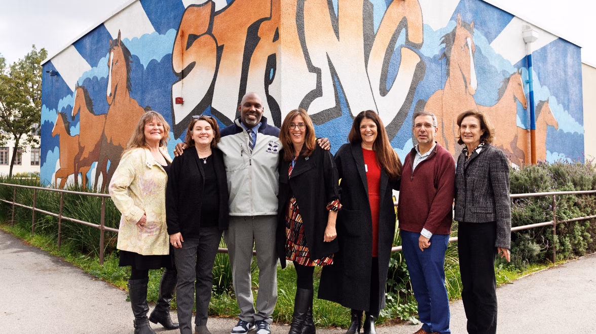 A group of 7 adults stand before a huge blue and orange mural that says STANGS