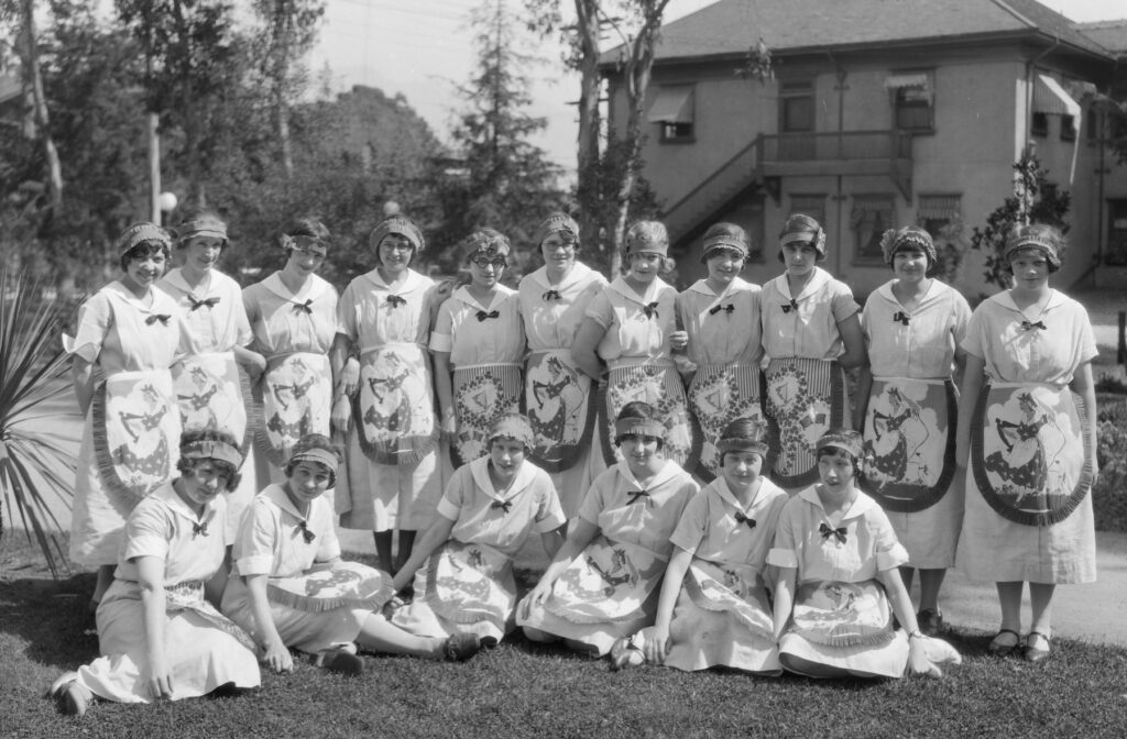 A black and white photo shows a large group of nurses in white uniforms outdoors on a lawn
