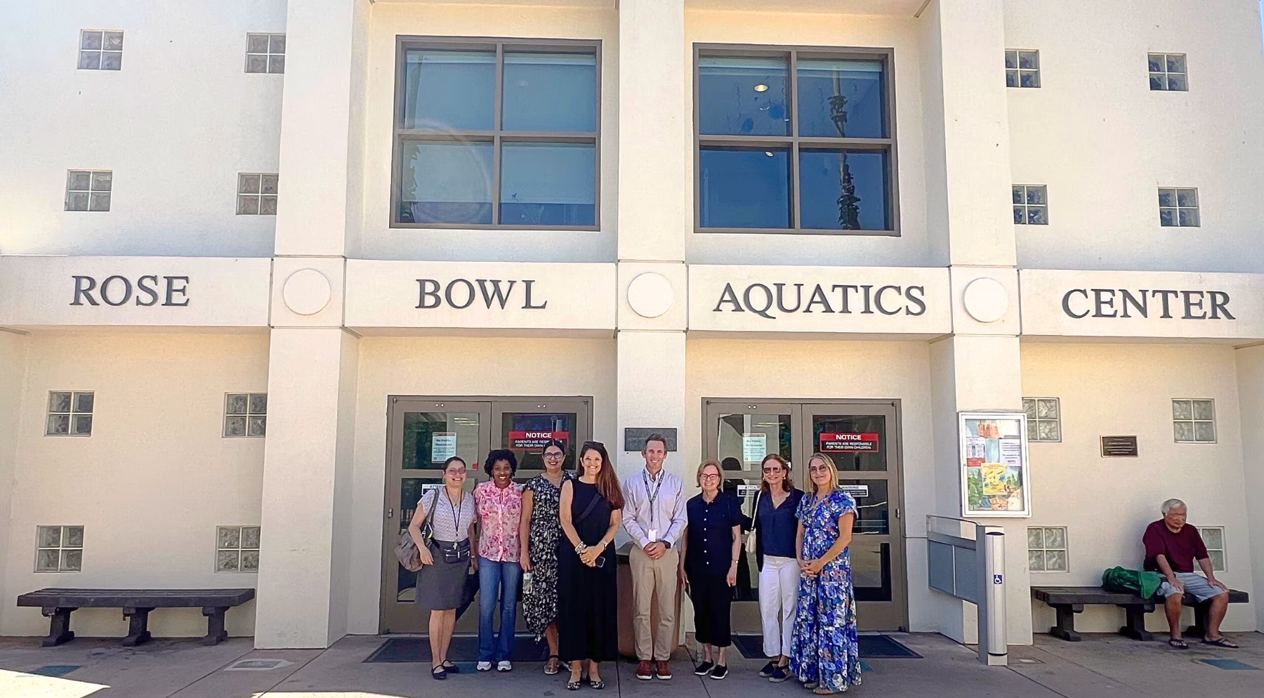A group of people stand outside doors to a building; above them the sign reads Rose Bowl Aquatics