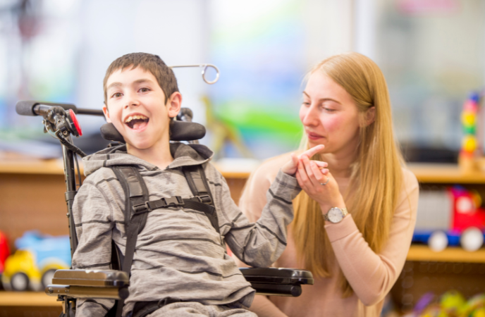 A young boy in a wheelchair inside a classroom with a teacher