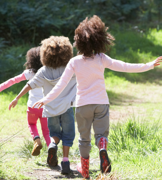 Three children run together up an outdoor path with their arms extended wide