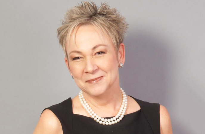 A headshot of an middle age white woman who has short cropped hair and is wearing a string of pearls and a black dress