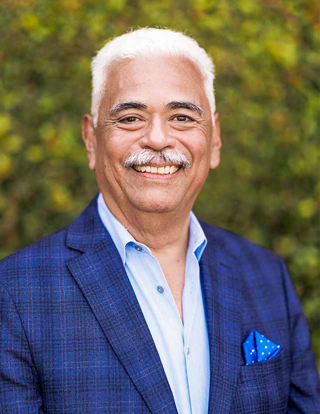 A man in a blue suit is smiling. Green leaf background.