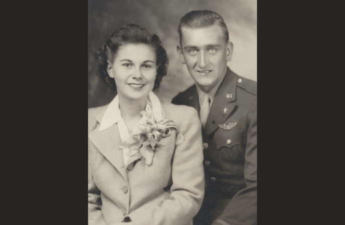 A vintage black and white portrait of a young man in a military suit and a young woman in a dressy suit with a corsage