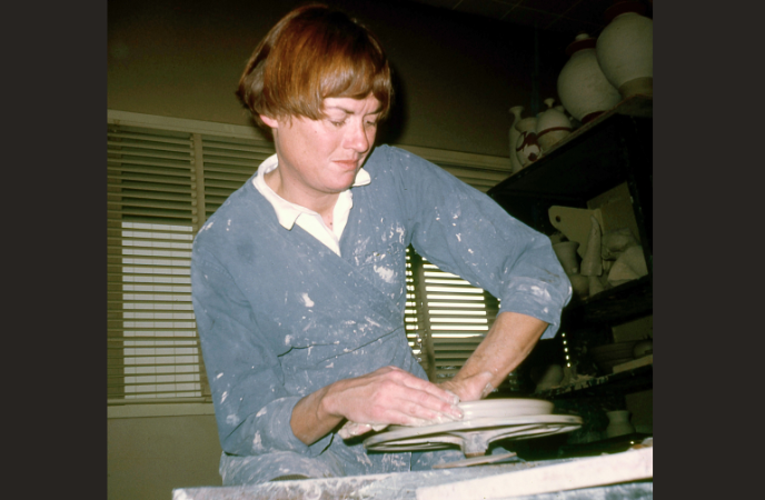 A vintage photo shows a young woman throwing a platter on a pottery wheel