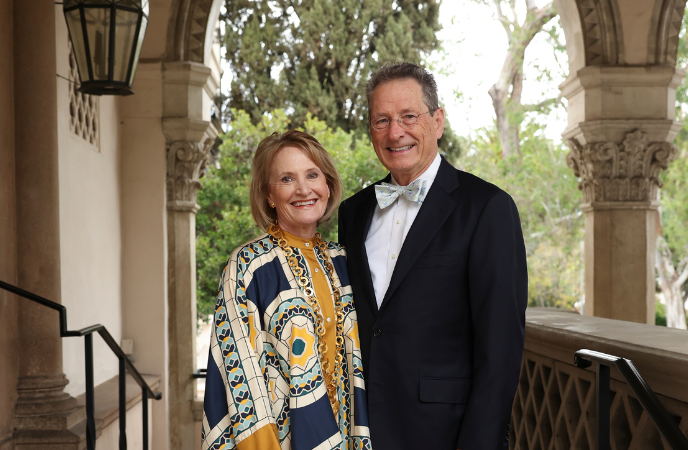 An older couple dressed in black tie attire stands under an arch