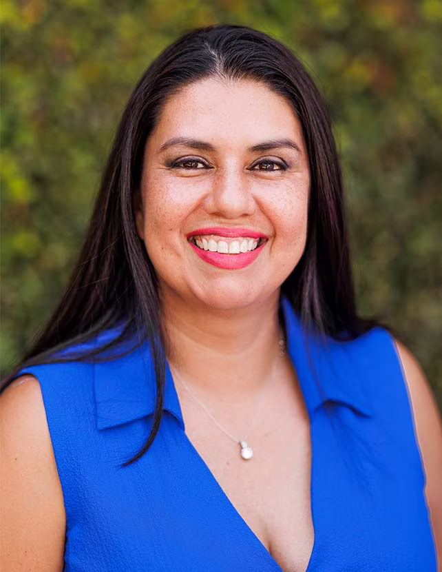 A woman is smiling in a blue shirt. Green leaf background.