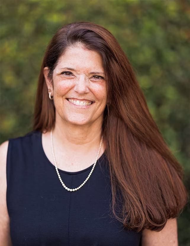 A woman in a black shirt is smiling. Green leaf background.