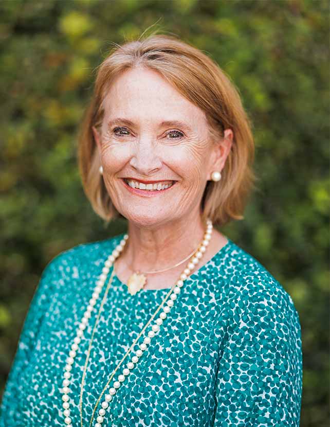 A woman in a floral blue shirt is smiling. Green leaf background.