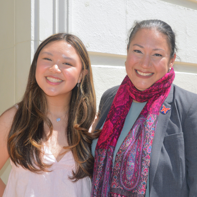 A young Asian women stands smiling with an older woman outdoors