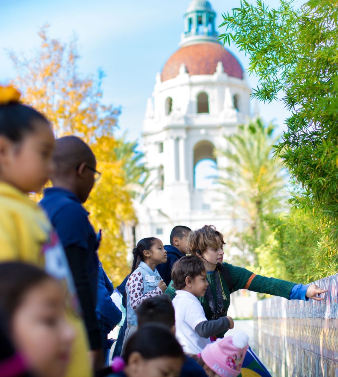 Group of kids pointing at a wall with the Pasadena City hall behind them