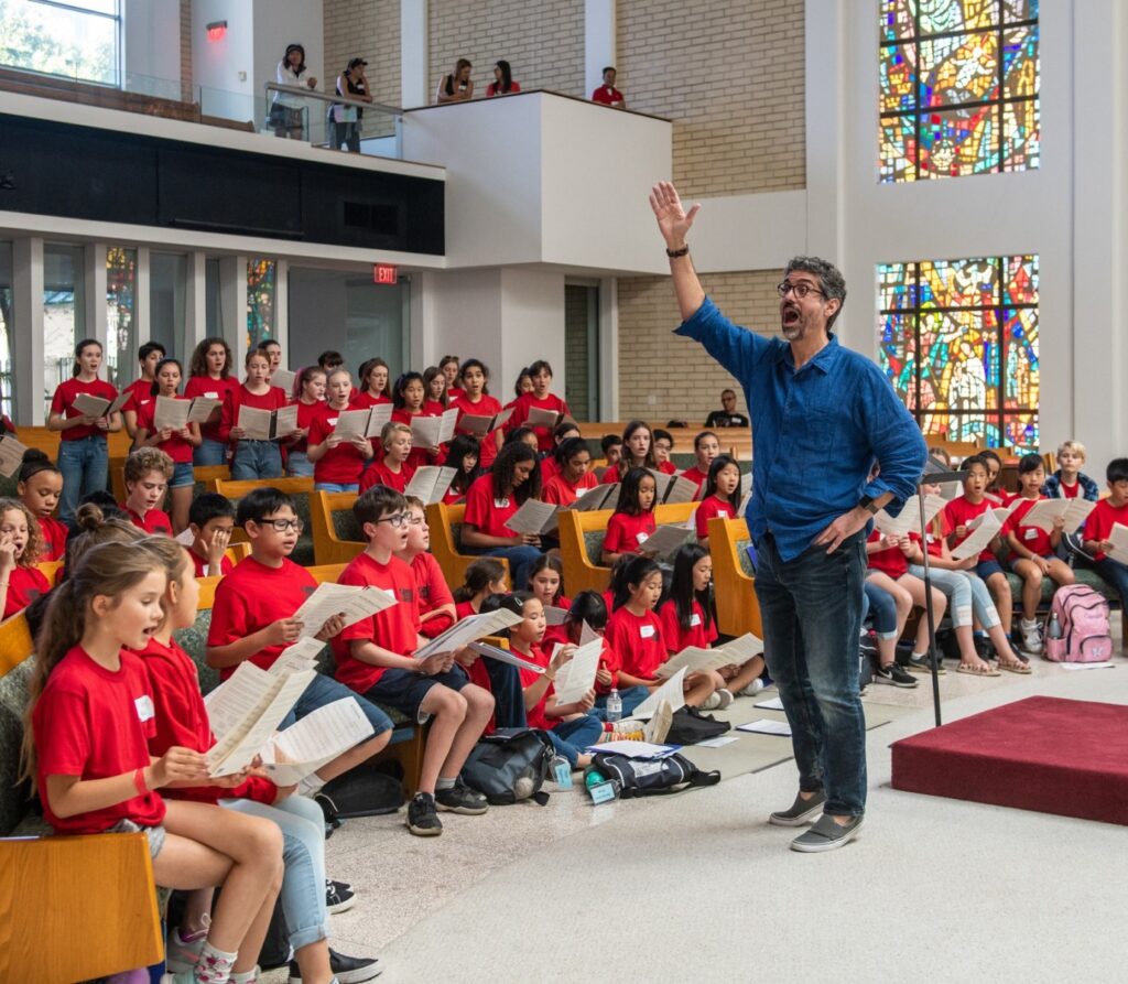 Man constructing a group of youth kids as they sing