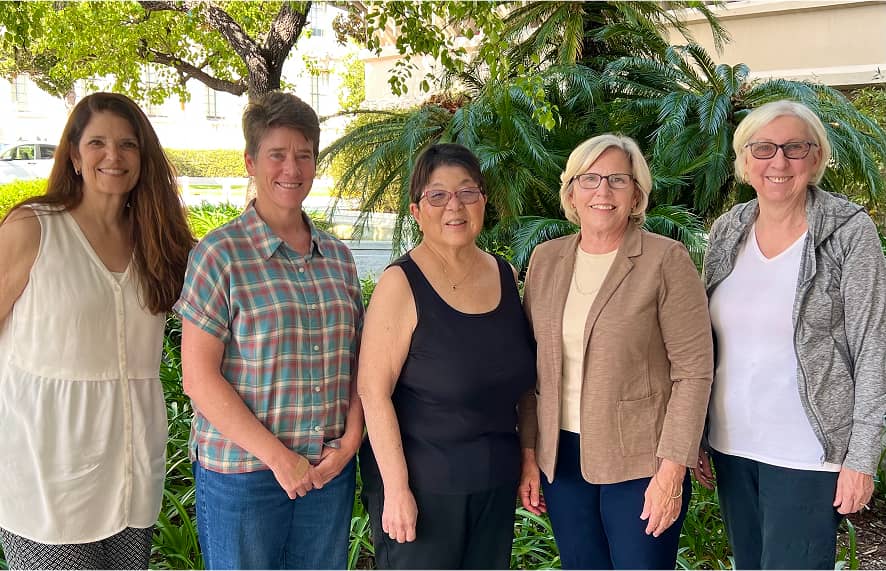5 women smiling for a photo outside under a tree