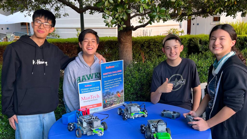 Four kids standing at a robotics table smiling