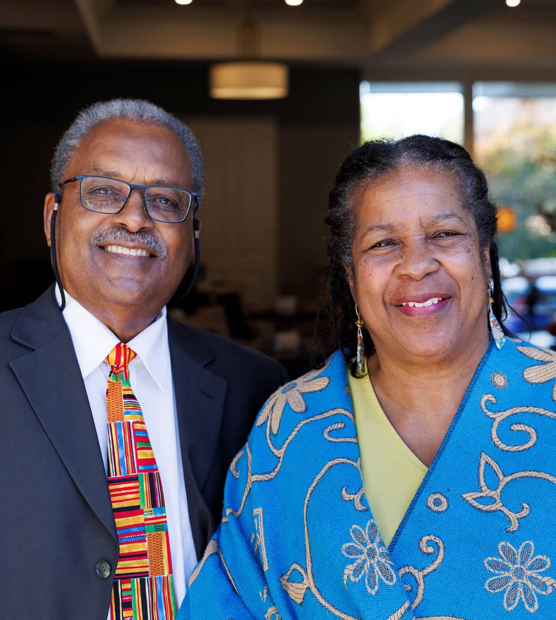 Two people, man and a woman, smiling for a photo. The woman is wearing a bright blue cover