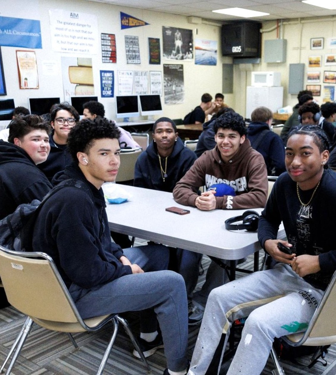 Classroom of students sitting at group table desks smiling at camera