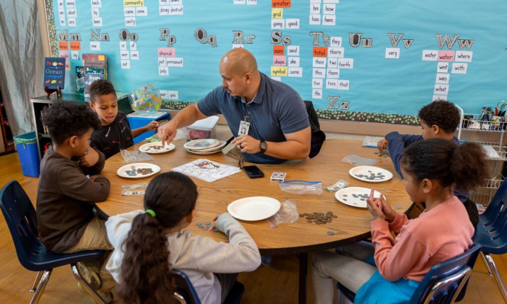Teacher sitting with group of kids at a large desk