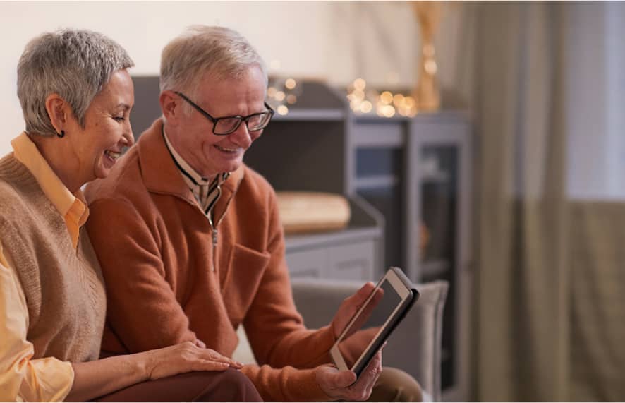 Older couple sitting and smiling at a tablet