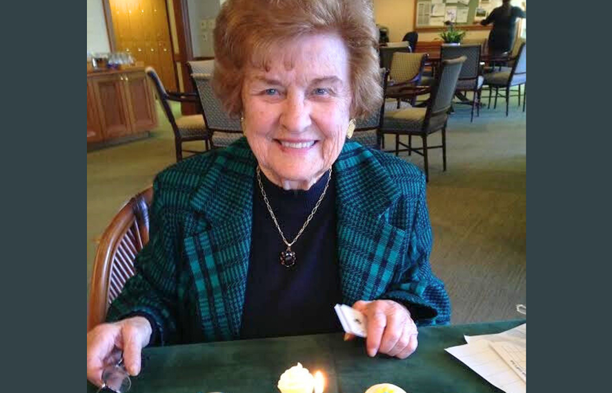 An older woman smiling at for a photo with a birthday cupcake candel lit