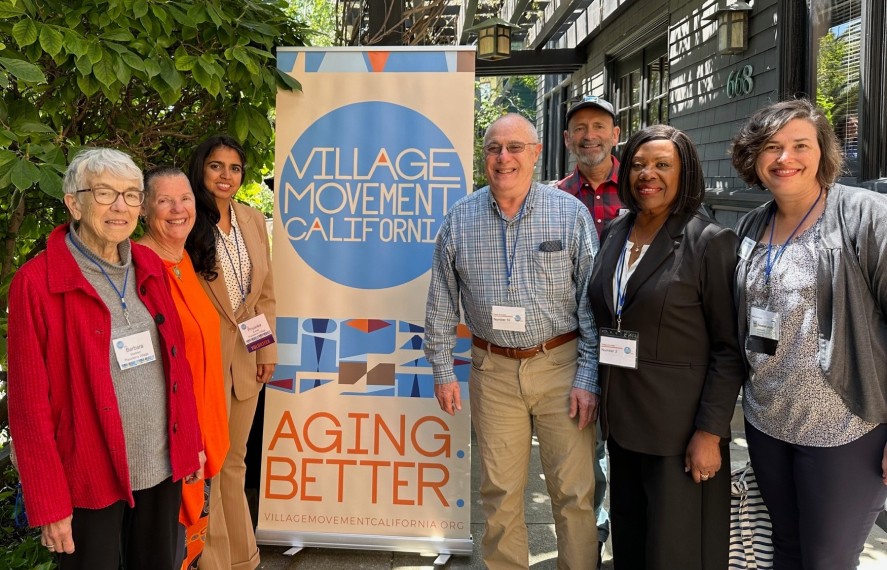Group of adults posing for a photo infront of the Village movement California standing sign
