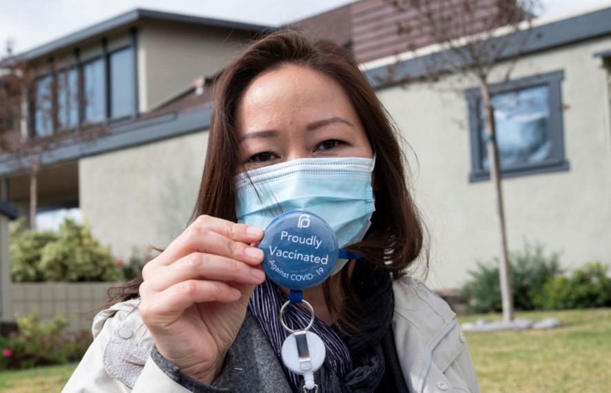 Nurse holding up lanyard pin that says 'Proudly Vaccinated'