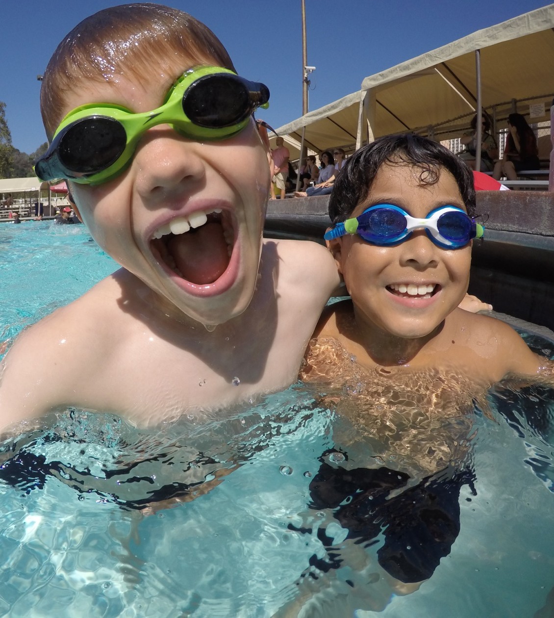 Two young boys in pool laughing with goggles on