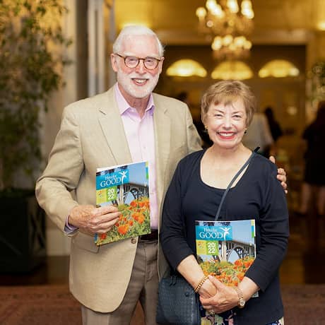 A man and woman smiling for a photo at an inside event with magazines in hand