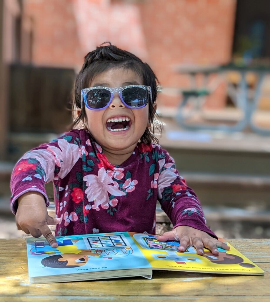 Little girl laughing with sunglasses on pointing at a book