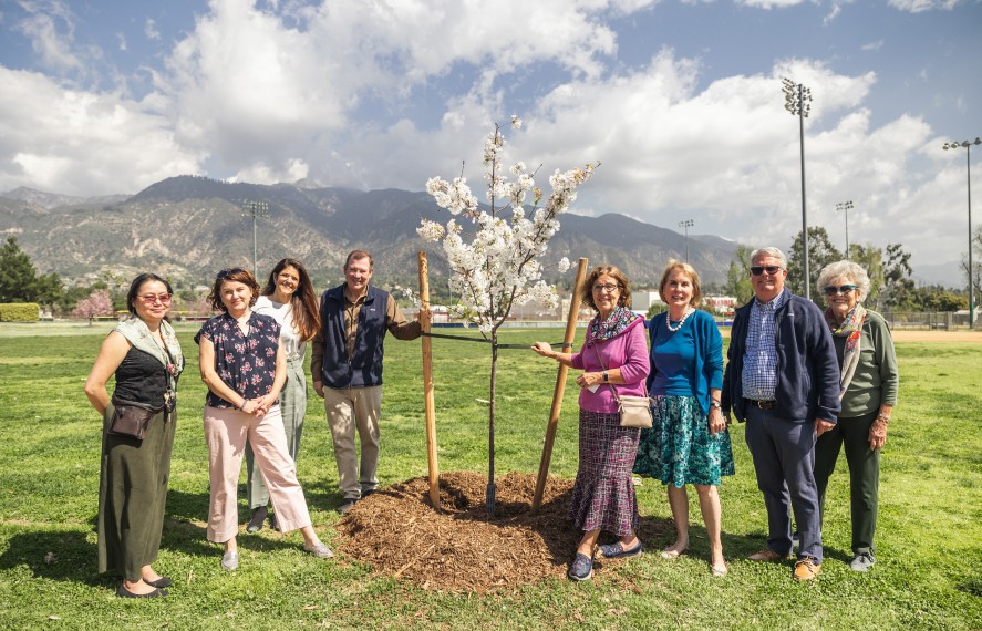 Group of people posing for an image next to a freshly planted white leaf tree