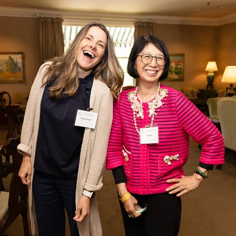 Two women laughing and posing for a photo at an event with name tags on
