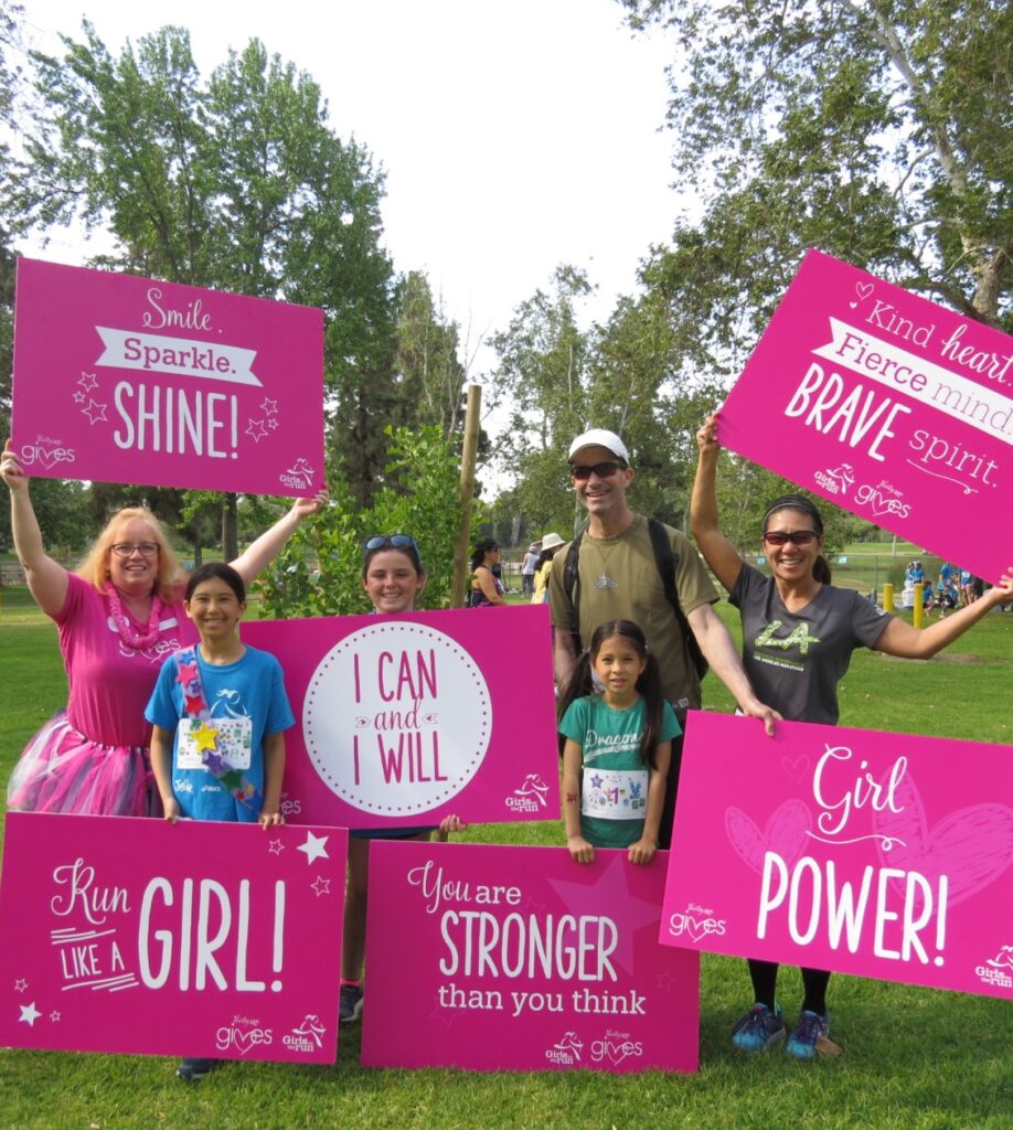 Three adults and three kids holding pink signs
