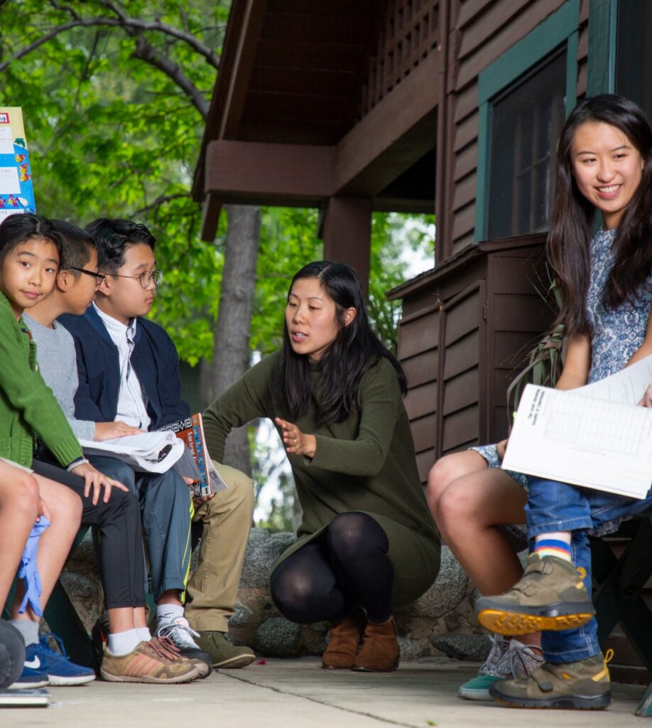 Two adults talking to students at a cabin like building