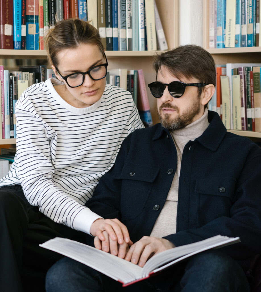 woman helping a blind man read braille