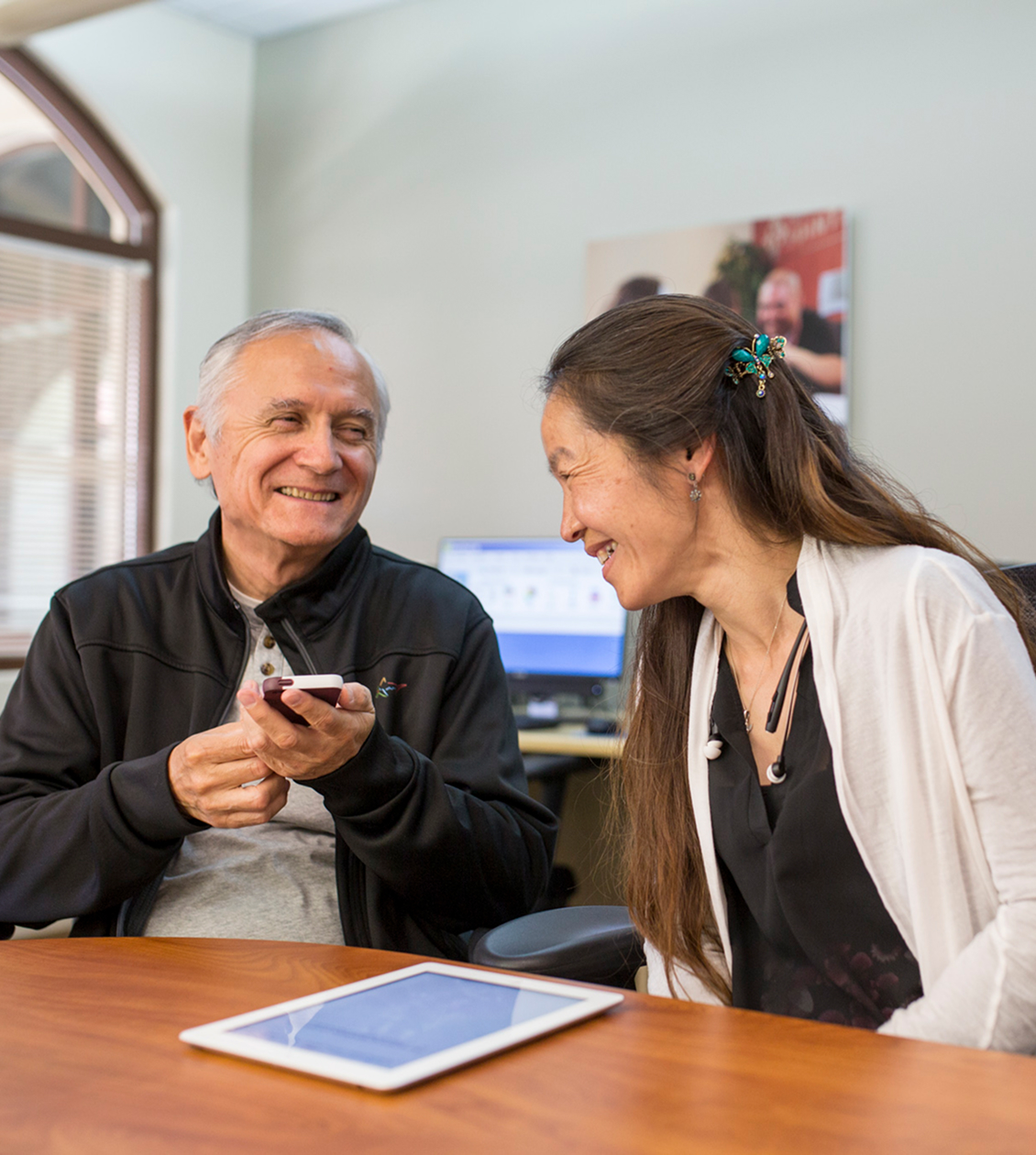 Older man and lady smiling in an office with a phone and tablet