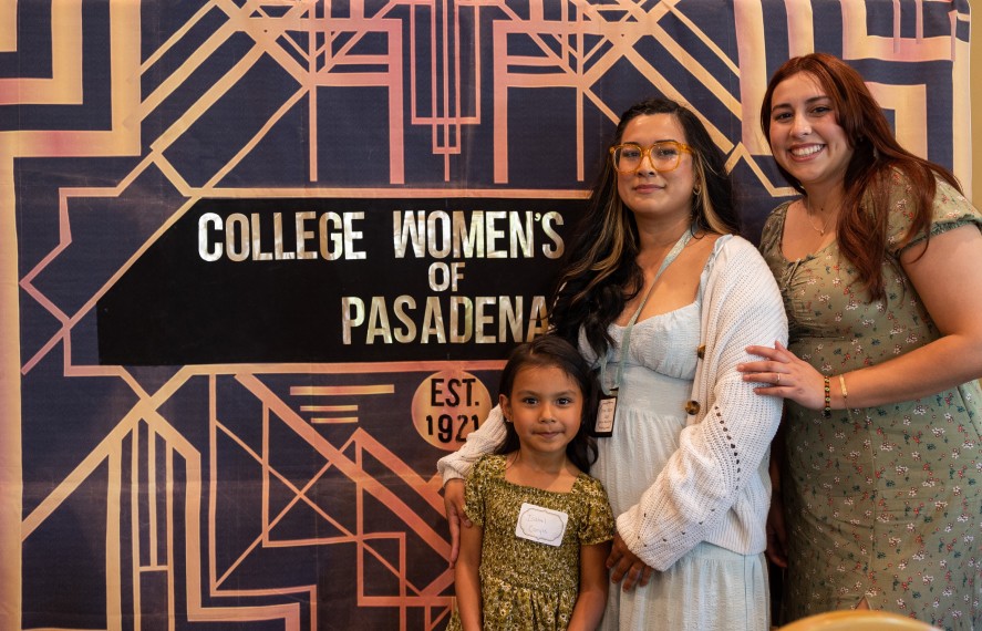 Two women and a young girl taking a photo in front of the College Women of Pasadena (Great Gatsby) sign