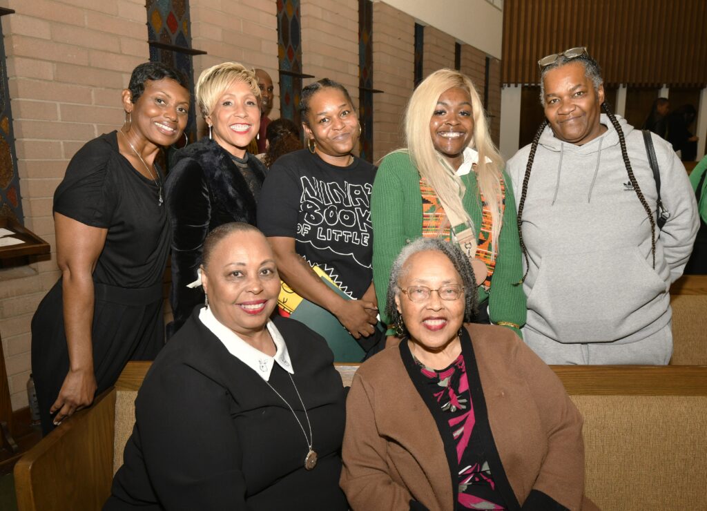A group of seven African American women sit and stand together as a group smiling at the camera