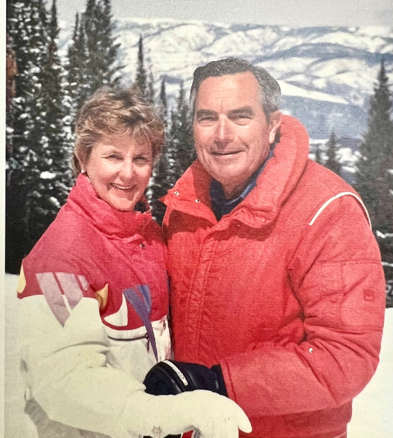 A vintage color photo shows a couple in ski gear with a mountain backdrop
