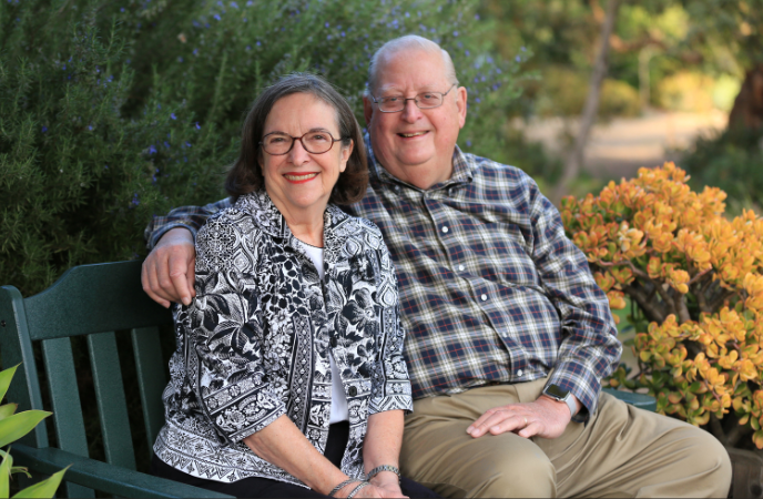 An older couple sits together on a park bench