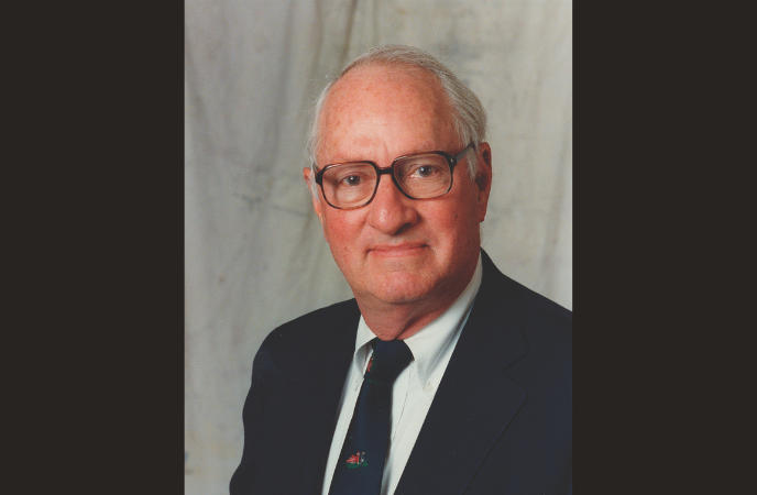 A headshot portrait of an older balding white man in a dark suit