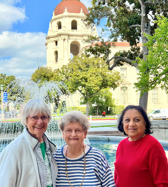 Three older women stand before an outdoor decorative fountain with Pasadena CA City Hall in background