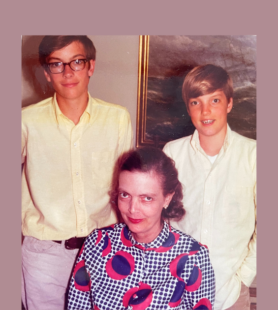 A 1960s era photo with a mother seated, wearing a colorful dress, and two teen boys standing behind her