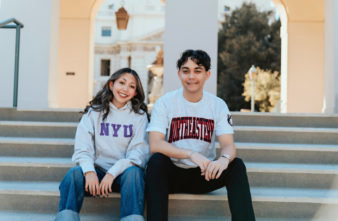 A young woman and man sit together on the steps of a civic building
